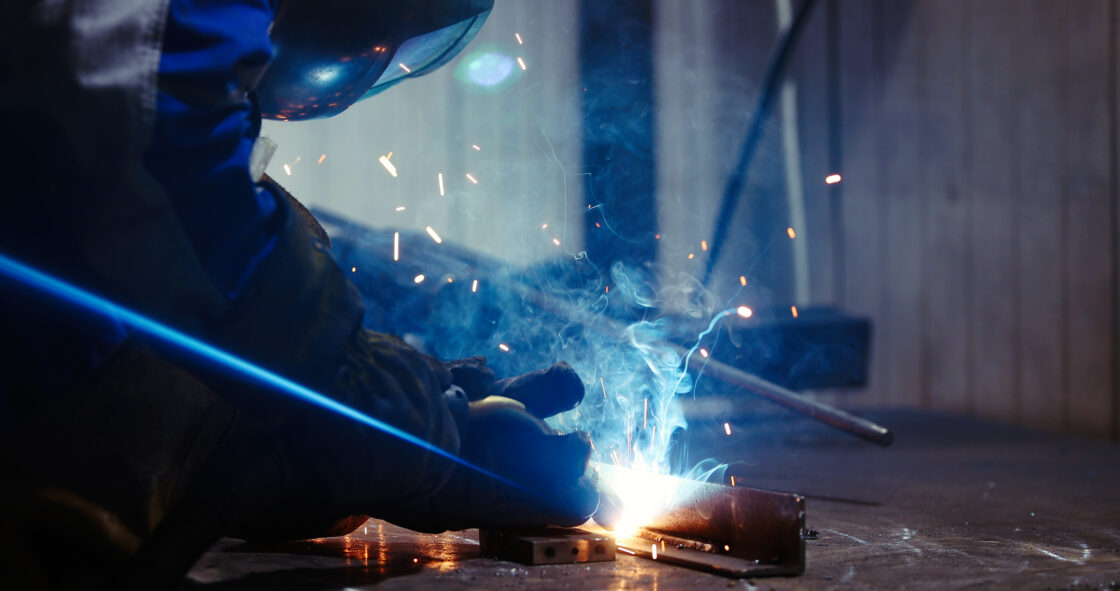 Imagem de uma pessoa soldando uma peça em uma metalúrgica