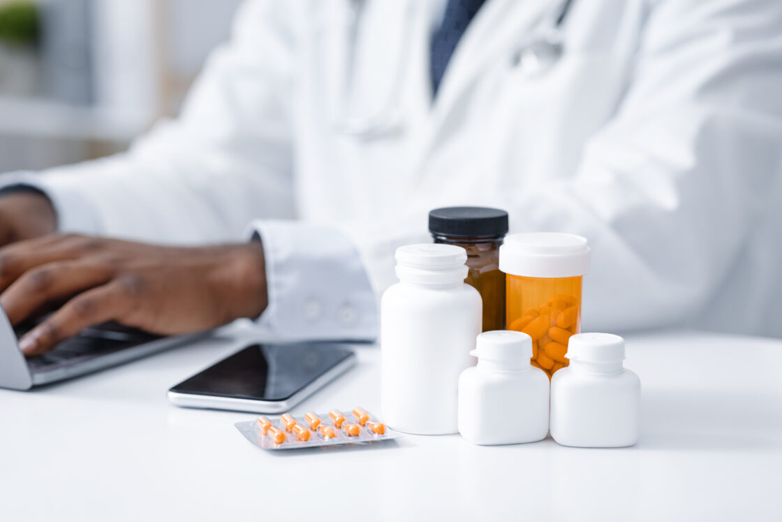 Imagem de medicamentos e comprimidos em frascos, com médico ao fundo usando um ERP para indústria química, ilustrando o tema de medicamentos e saúde.