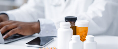 Imagem de medicamentos e comprimidos em frascos, com médico ao fundo usando um ERP para indústria química, ilustrando o tema de medicamentos e saúde.