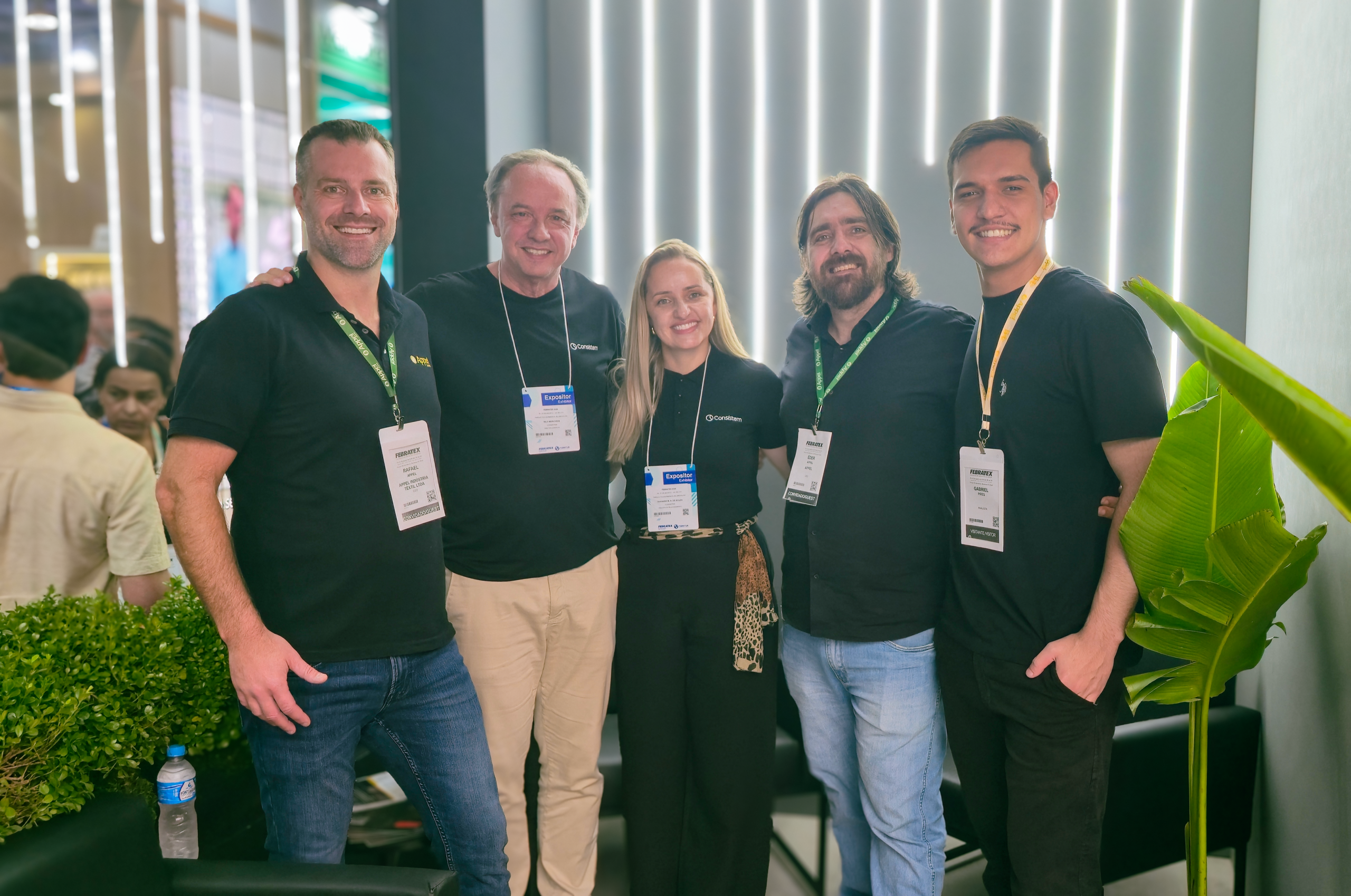 Cinco integrantes da equipe da Consistem e da Appel Home sorrindo lado a lado no estande da empresa durante a Febratex 2026, utilizando crachás do evento.