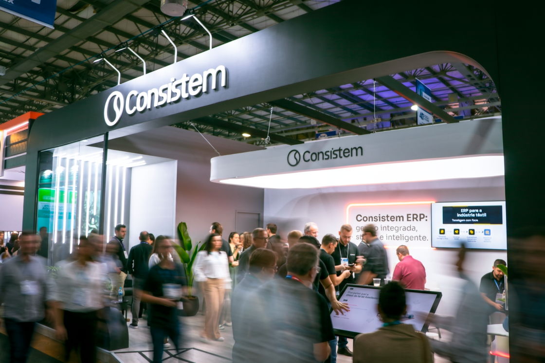Estande da Consistem na Febratex 2026 bastante movimentado, com visitantes e especialistas conversando, e painel ao fundo destacando "Consistem ERP: gestão integrada, segura e inteligente".