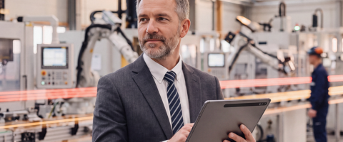 CEO e líder industrial em primeiro plano com fábrica moderna e dados de inteligência artificial ao fundo.